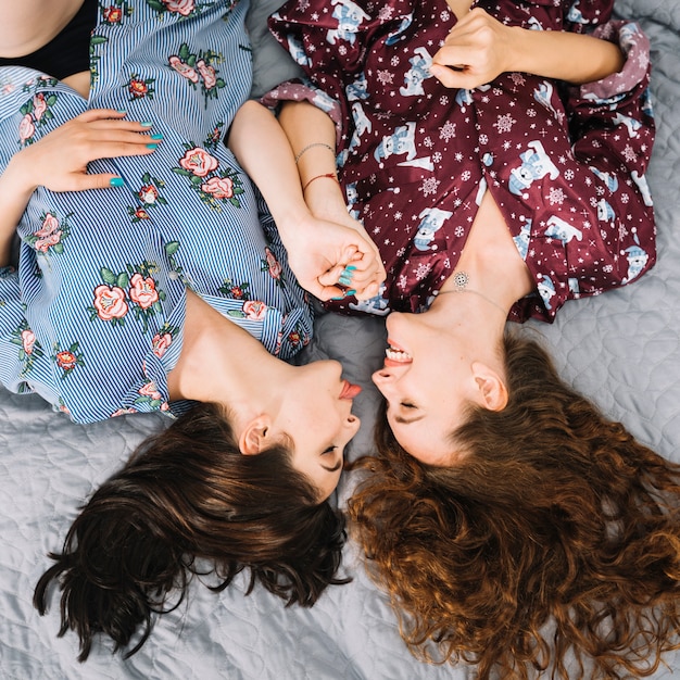 Two female friends lying on bed holding each others hand