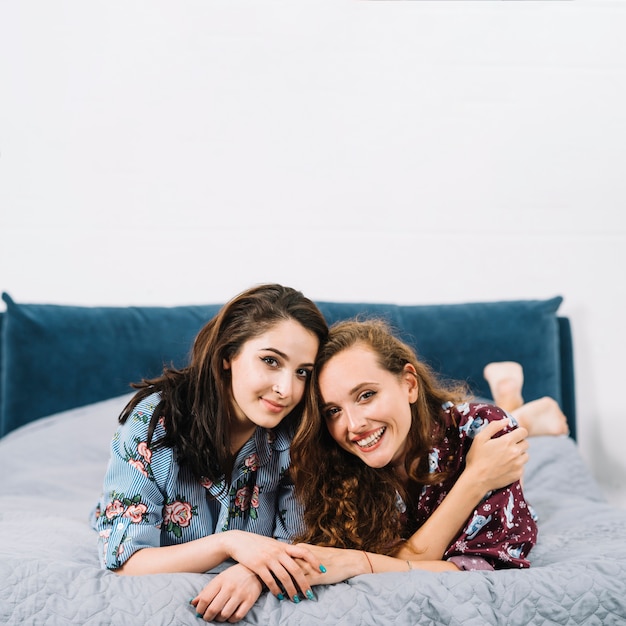 Two female friends lying on bed looking at camera