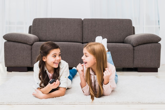 Two female friends lying on carpet making fun at home