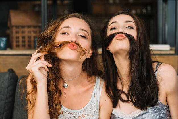 그들의 머리와 가짜 콧수염을 만드는 두 여자 친구
