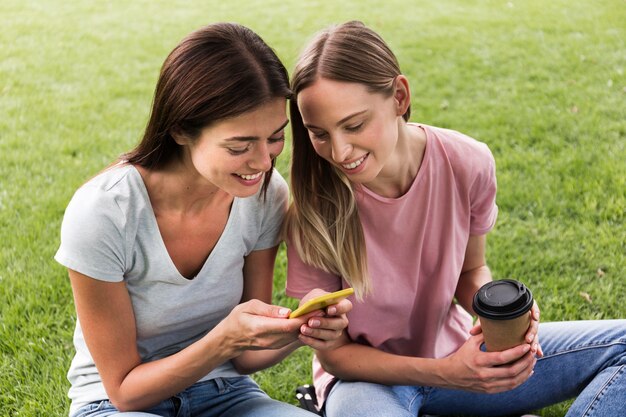 Two female friends outdoors with smartphone and coffee