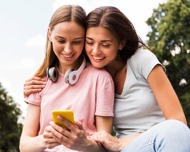 Two female friends outdoors with smartphone and headphones