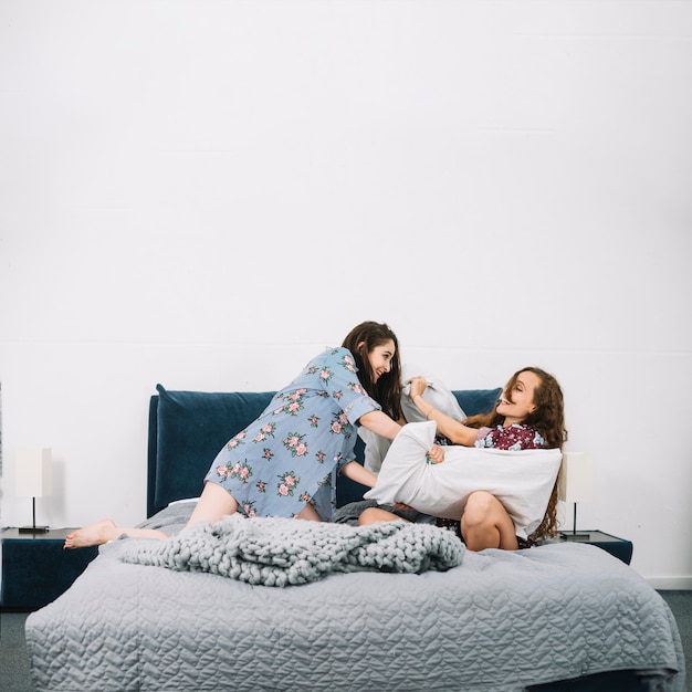 Free photo two female friends pillow fighting on bed