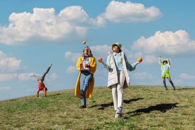 Two female friends playing with oranges and other two dancing in an outdoor field