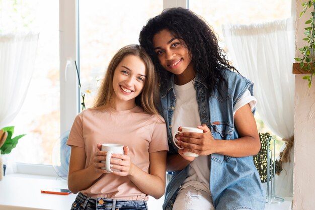 Two female friends posing together with mugs in the kitchen