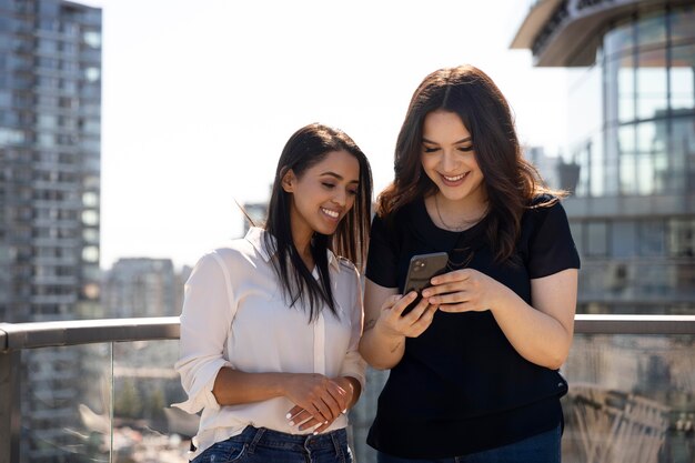 Two female friends at a rooftop terrace using smartphone