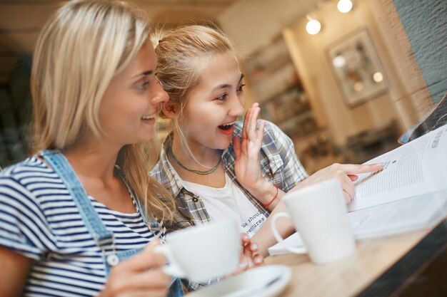 Two female friends sitting inside cafe and having coffee