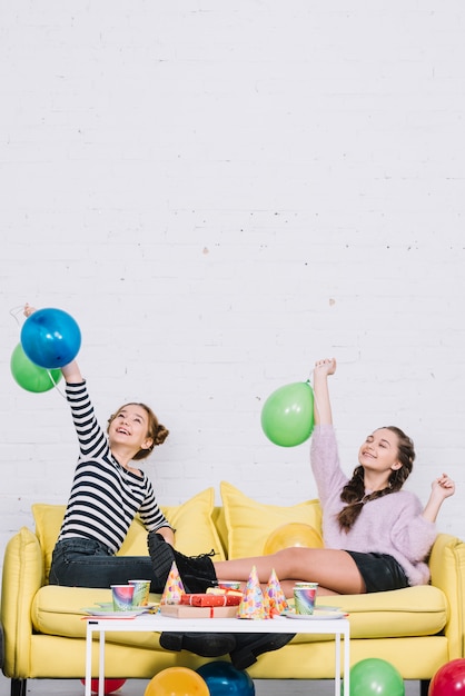 Two female friends sitting on sofa enjoying the birthday party at home