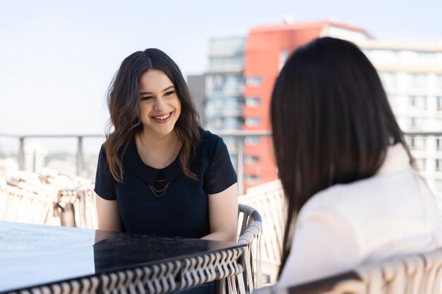 Two female friends spending time together and drinking wine on a rooftop terrace