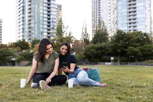 Two female friends spending time together at the park and using smartphone