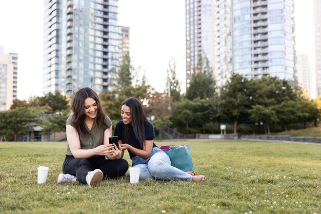 Two female friends spending time together at the park and using smartphone