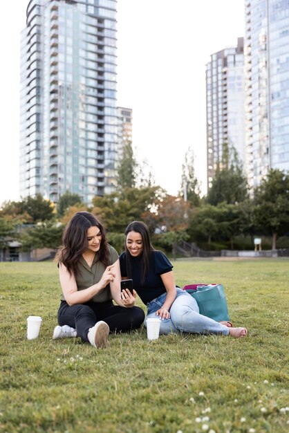 Two female friends spending time together at the park and using smartphone