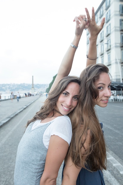 Two female friends standing on street raising their hands