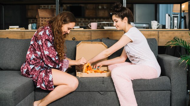 Two female friends taking pizza slices from box