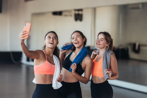 Two female friends taking a selfie photo after hard workout in gym.
