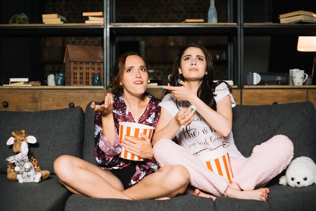 Two female friends watching television shrugging
