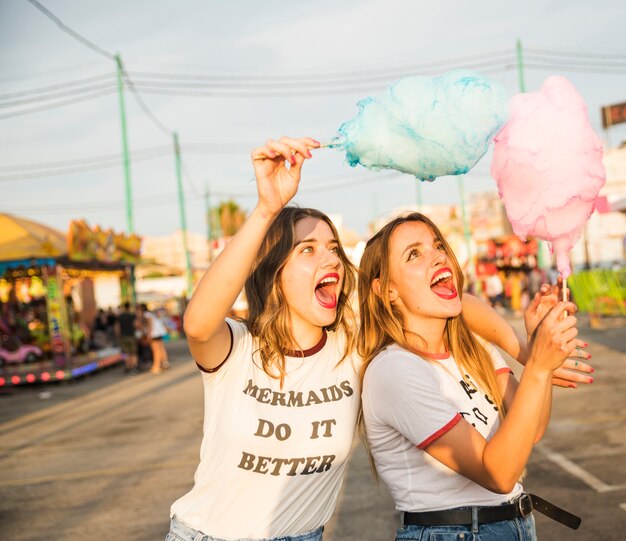 Two female friends with candy floss having fun at amusement park