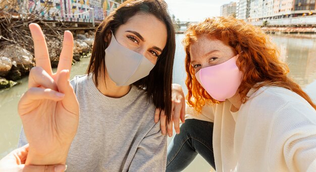 Two female friends with face masks outdoors taking a selfie together