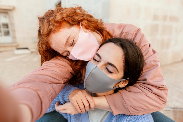 Free photo two female friends with face masks outdoors taking a selfie