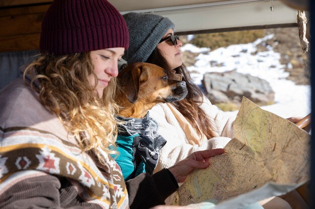 Two female lovers inside a camper van with their dog consulting a map for their winter trip