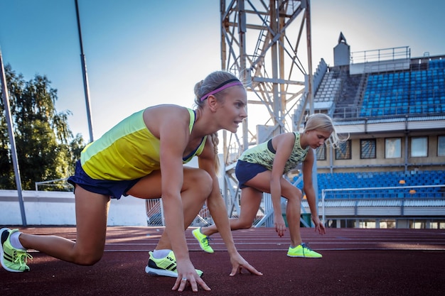 Foto gratuita due atlete velociste femminili che si preparano per iniziare una gara su una pista da corsa rossa nello stadio di atletica leggera.