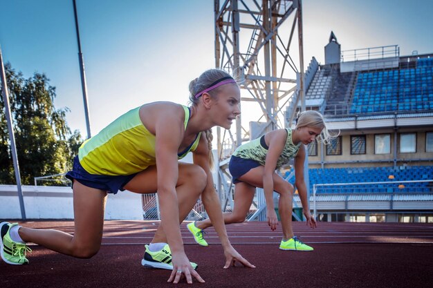 Two female sprinter athlete getting ready to start a race on a red running track in athletics stadium.