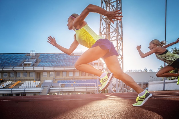 Two female sprinter athletes running on the treadmill race during training in the athletics stadium.