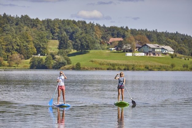 Two females riding a stand up paddle board in the Smartinsko lake in Slovenia