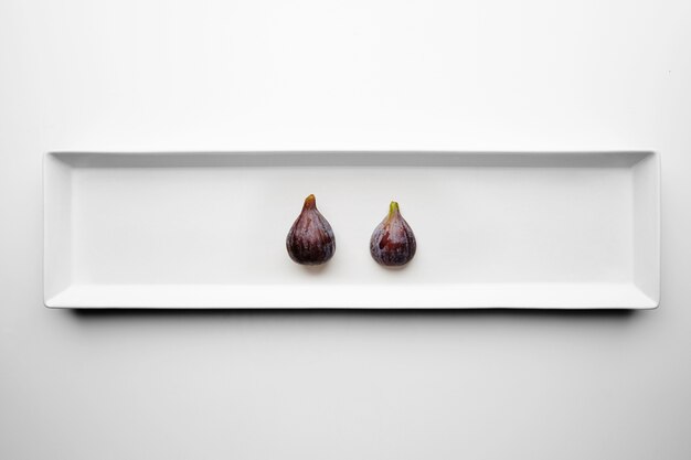 Two figs isolated in center rectangular ceramic plate on white table