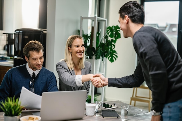 Two financial advisors having a meeting with young man at home Female advisor is shaking hands with a client