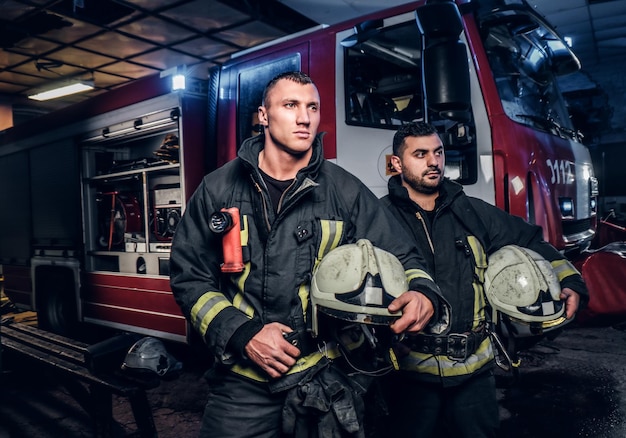 Двое пожарных в защитной форме стоят рядом с пожарной машиной. Прибытие по вызову в ночное время