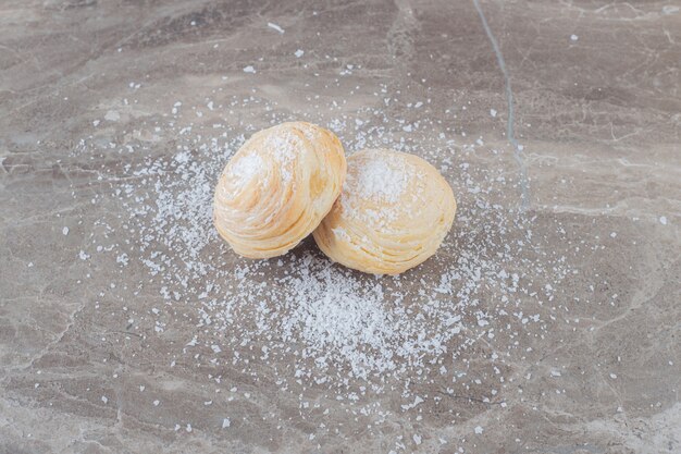 Two flaky cookies coated with vanilla powder on marble surface