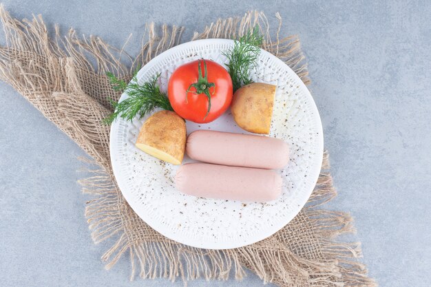 Two fresh boiled sausage on white plate with potato and tomato. 