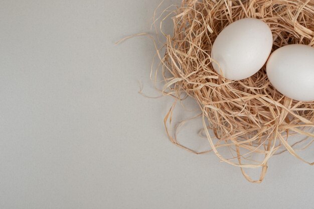 Two fresh chicken white eggs on hay .