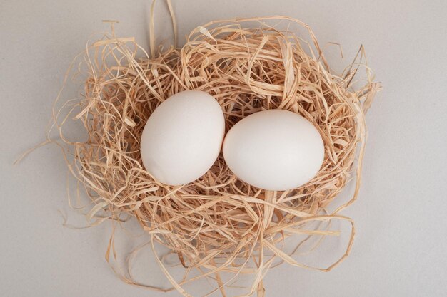 Two fresh chicken white eggs on hay .