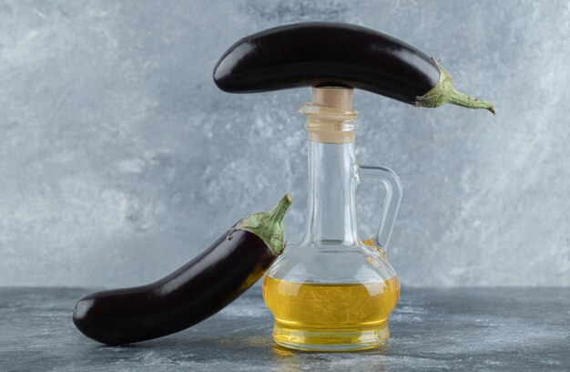 Two fresh eggplant with bottle of oil on grey background.
