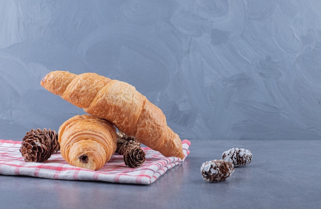 Two fresh French croissant with decorative pine cone.