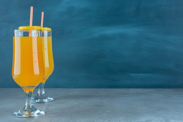 Два свежих фруктовых сока в стеклянных стаканчиках с соломинкой.
