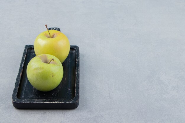 Two fresh green apples on black plate. 