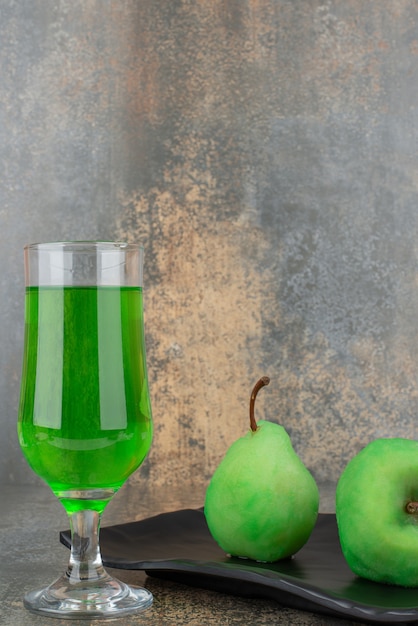 Два свежих зеленых яблока со стаканом зеленой воды на темной тарелке