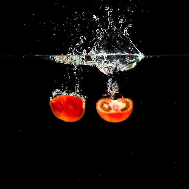 Two fresh halved red tomatoes falling into water