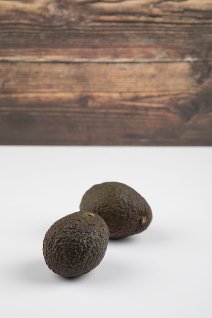 Два свежих здоровых коричневых авокадо, изолированные на бело-сером фоне.
