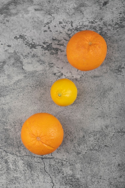 Two fresh orange fruits with whole lemon on stone table.