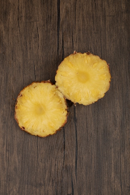 Two fresh ripe pineapple slices placed on a wooden table. 