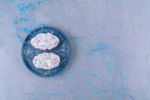 Two fresh sweet cupcakes with colorful sprinkles and cream on a blue wooden board. 