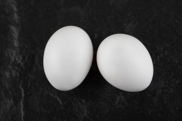 Two fresh white chicken eggs on a black table . 