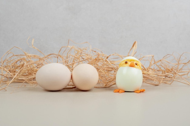 Two fresh white chicken eggs with chicken toy and hay .