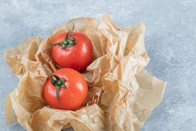 Two fresh whole tomatoes on a parchment paper. 