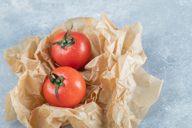 Two fresh whole tomatoes on a parchment paper. 