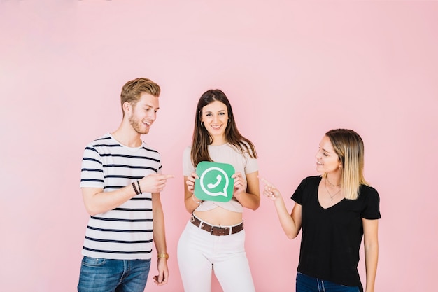 Two friends pointing at smiling woman holding whatsapp icon